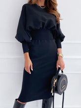 Load image into Gallery viewer, Classy, comfortably soft jersey dress. Dolman sleeves that allows for a baggy fit on the top of the sleeves through the top half of the dress. Waist line is cinched with an wide band elastic waist of the same material, blending into the overall look of the dress. The forearm sleeves are comfortably snug and fashionably stop above the wrist. The bottom half of the dress is a pencil skirt fit. Model is accessorizing with black knee boots and a black purse in hand, with a gold watch.
